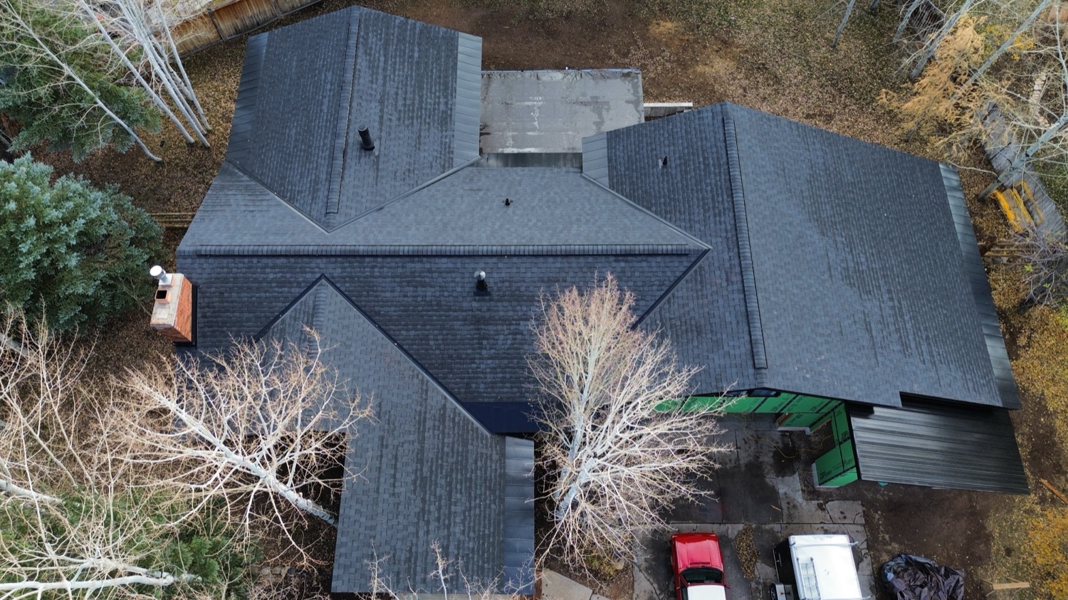 Aerial view of a finished dark architectural shingle roof surrounded by autumn trees