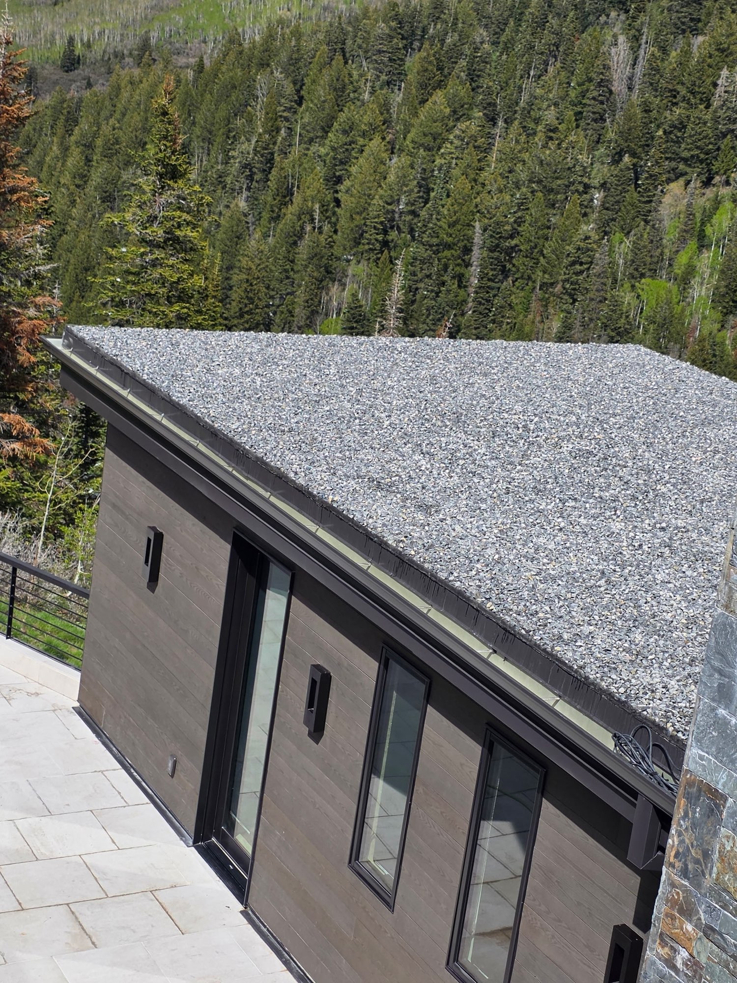 Ballasted gravel flat roof with custom dark metal gutter on a mountain home in Utah