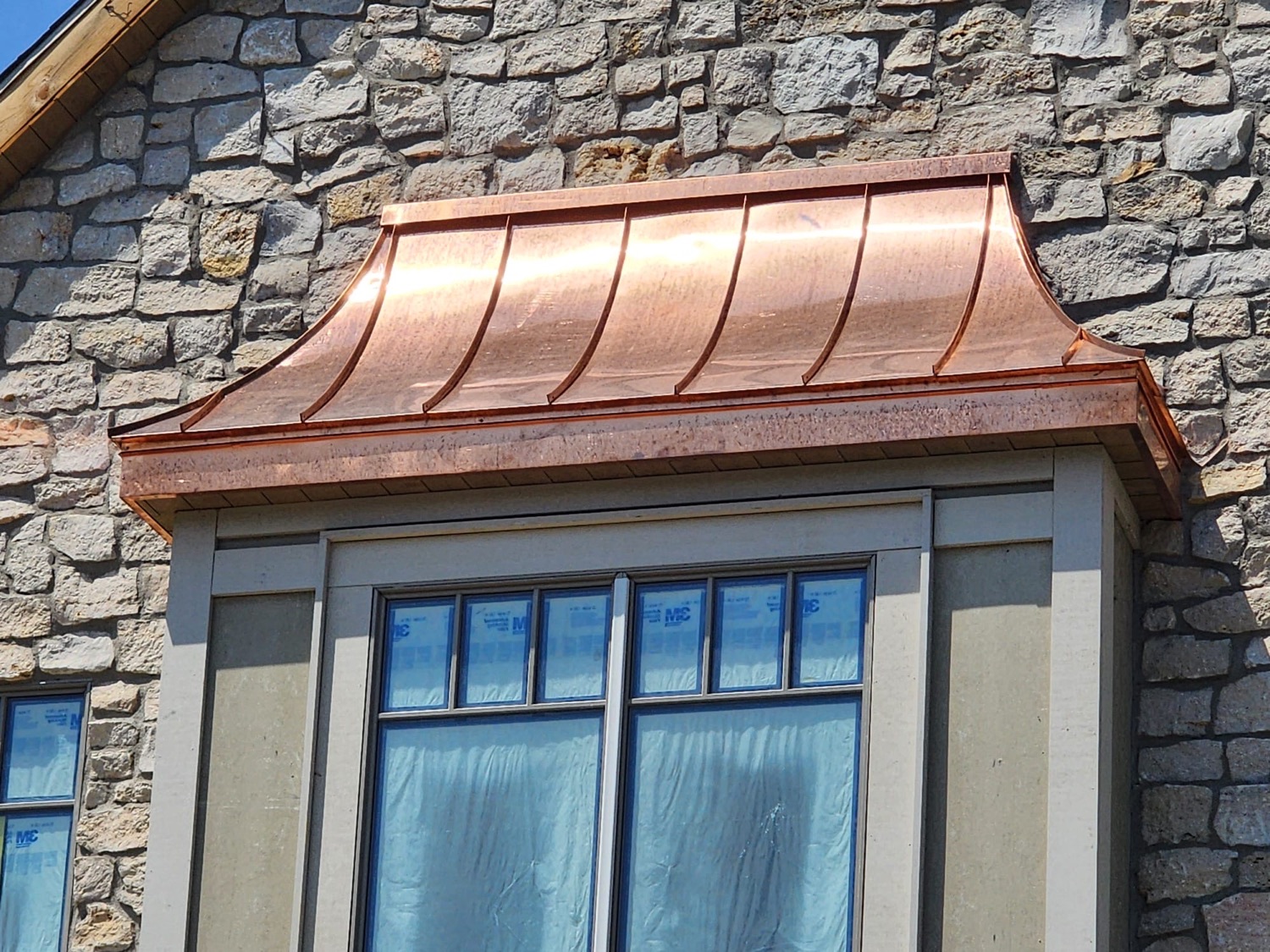 Custom copper bay window roof and fascia on a stone home