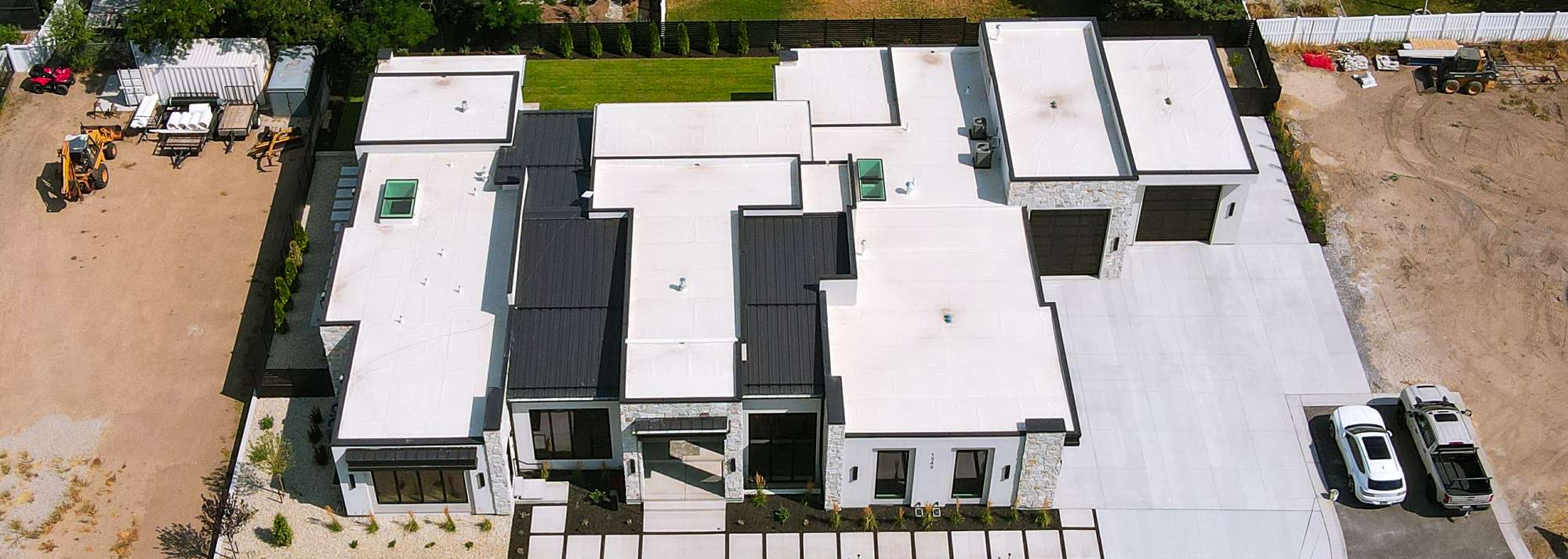 Aerial view of a large modern Utah home with a new white TPO membrane flat roof and dark standing-seam metal accents