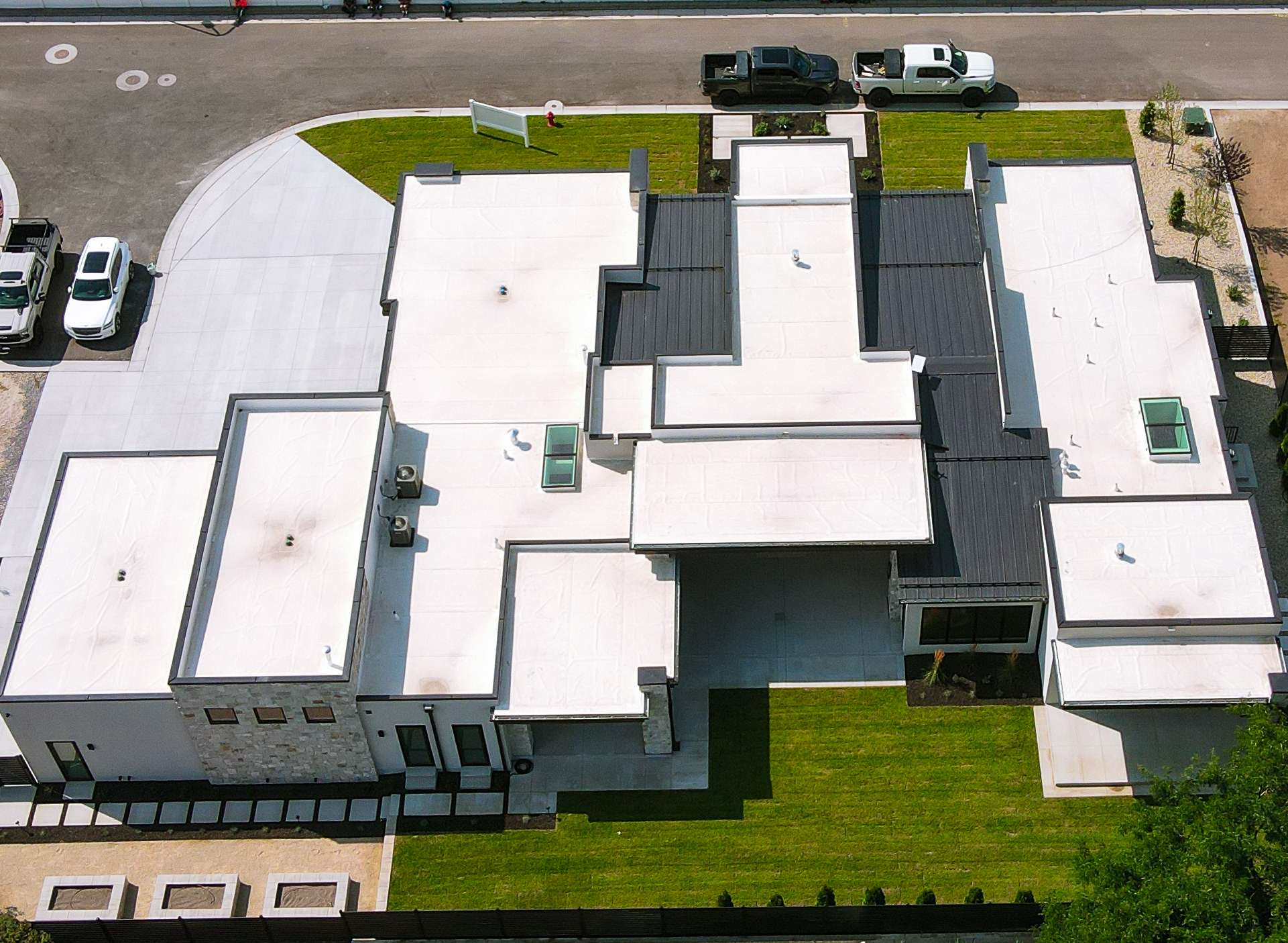 Top-down aerial view of a modern custom home showing white flat membrane roofing and dark standing-seam metal detail