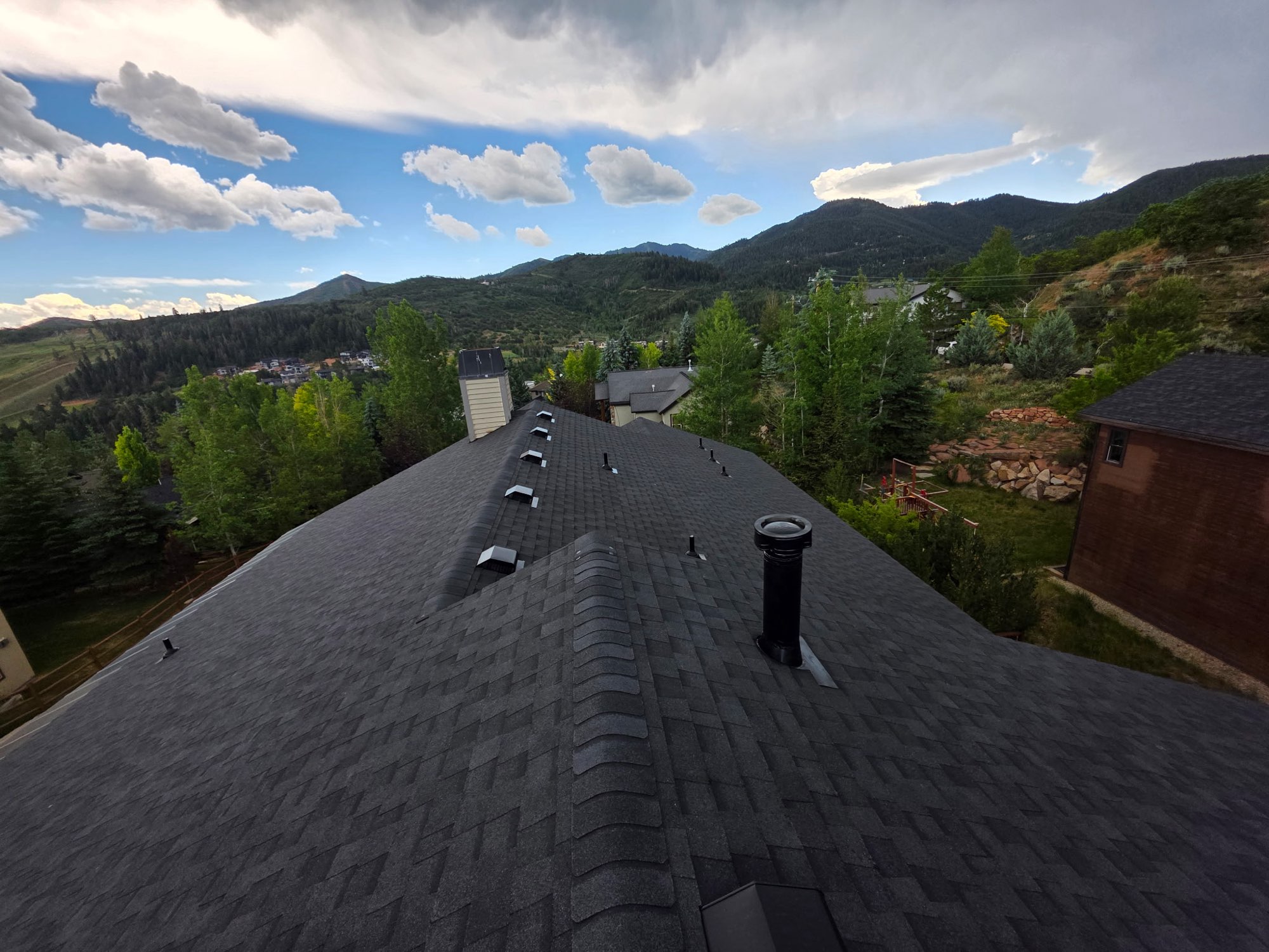 Completed roofing project in Utah with a new charcoal shingle roof and vents above a mountain valley